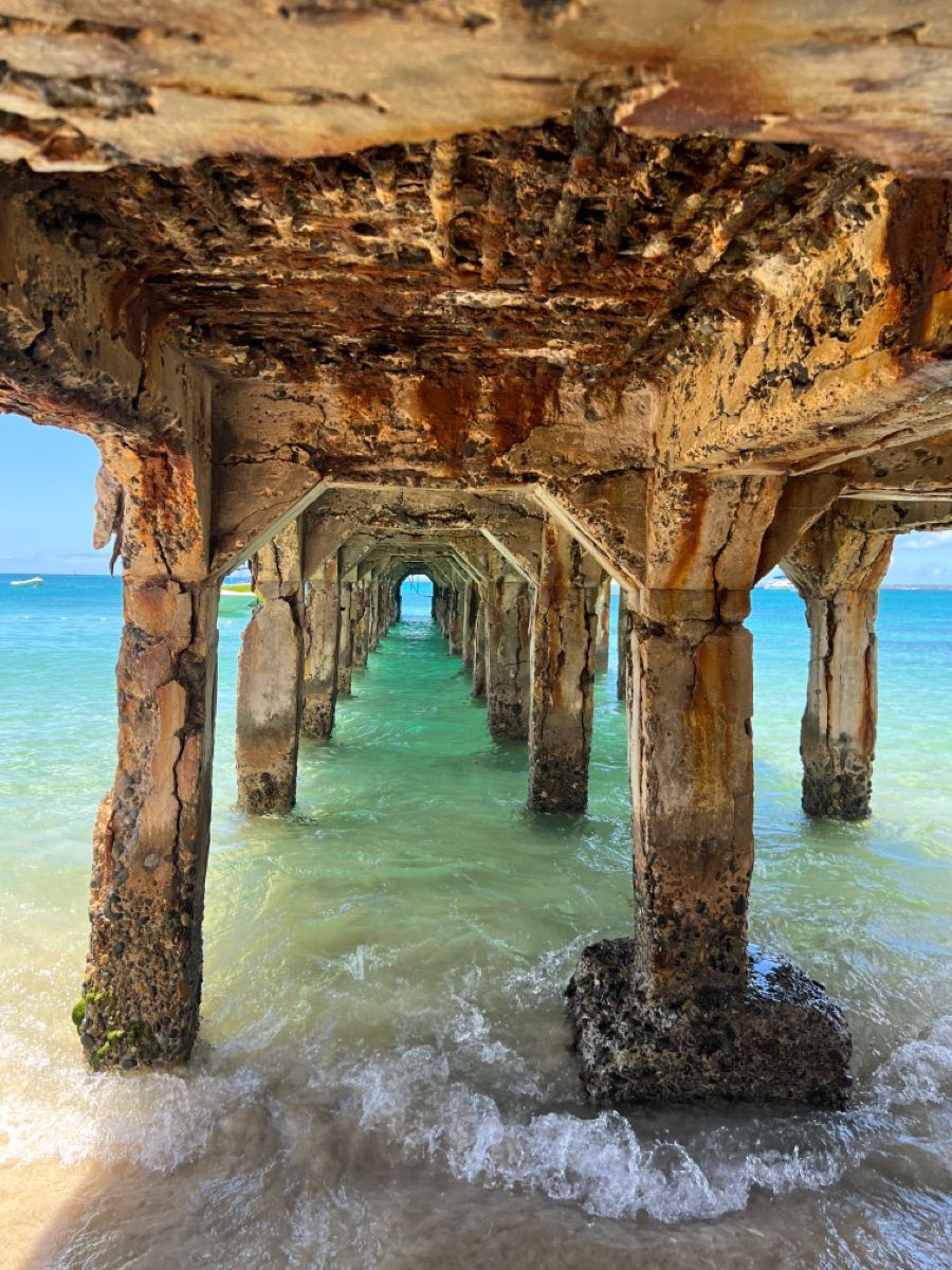 Turquoise water seen through the weathered pillars beneath a Sint Maarten pier